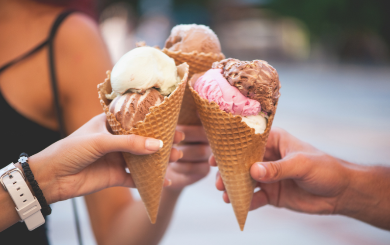 Three ice cream cones held up in a toast, with flavors including vanilla, chocolate, and strawberry.
